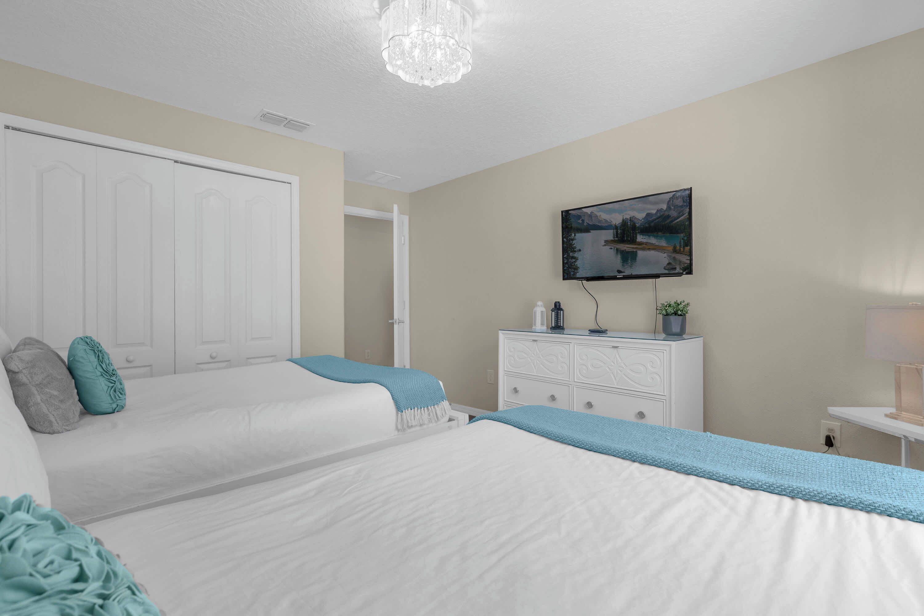 Une chambre avec deux lits, une commode, un téléviseur et un tableau au mur.