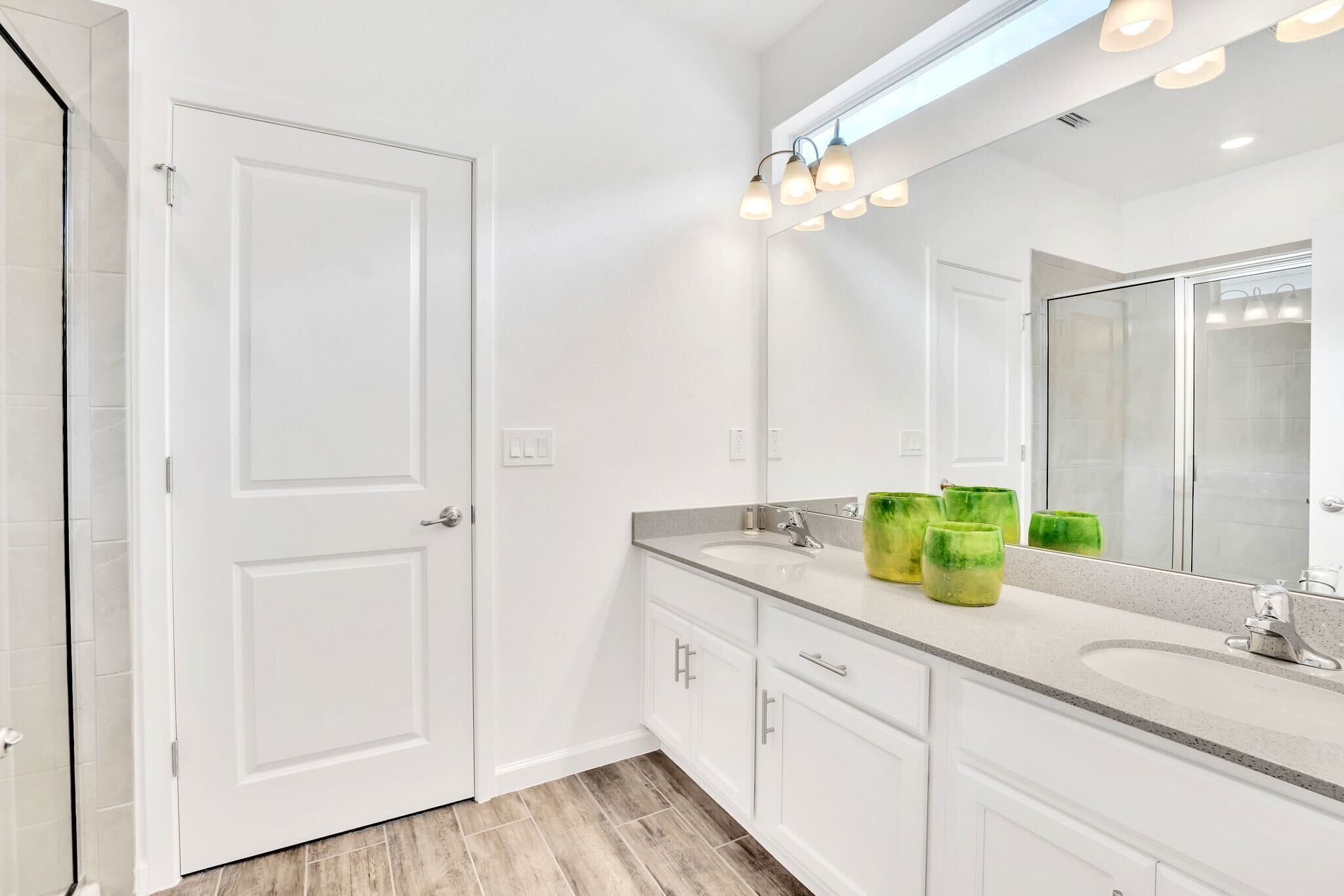 A modern bathroom with a large mirror, white cabinetry, and a countertop with green vases.