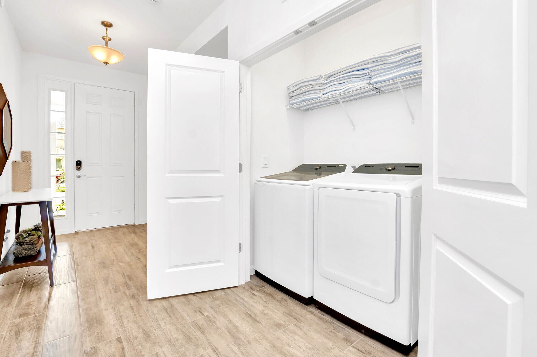 A laundry room with a white door, two washing machines, a ceiling light, and a wall-mounted laundry rack.