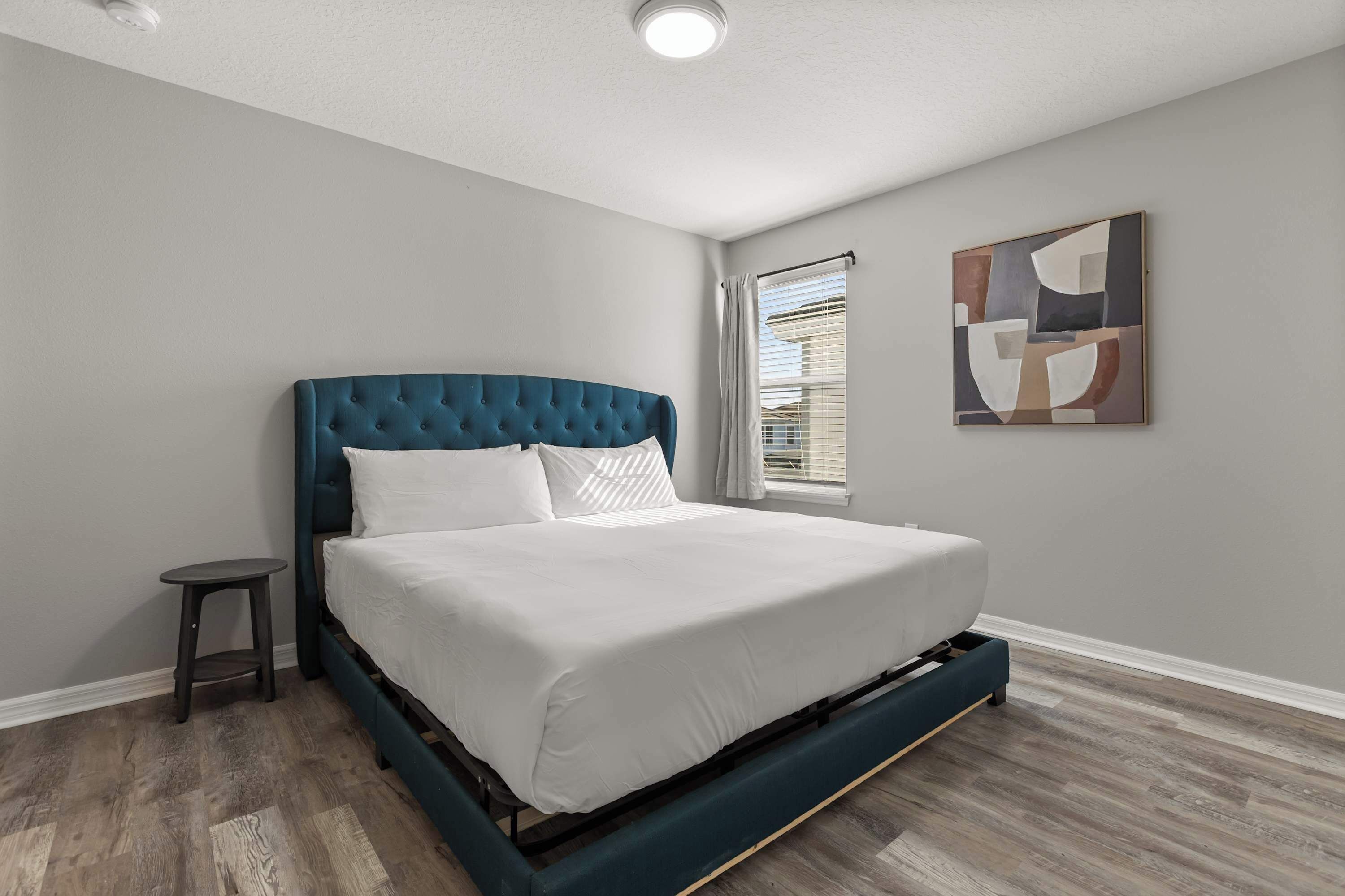 A bedroom with a bed, a small stool, and a window with blinds.