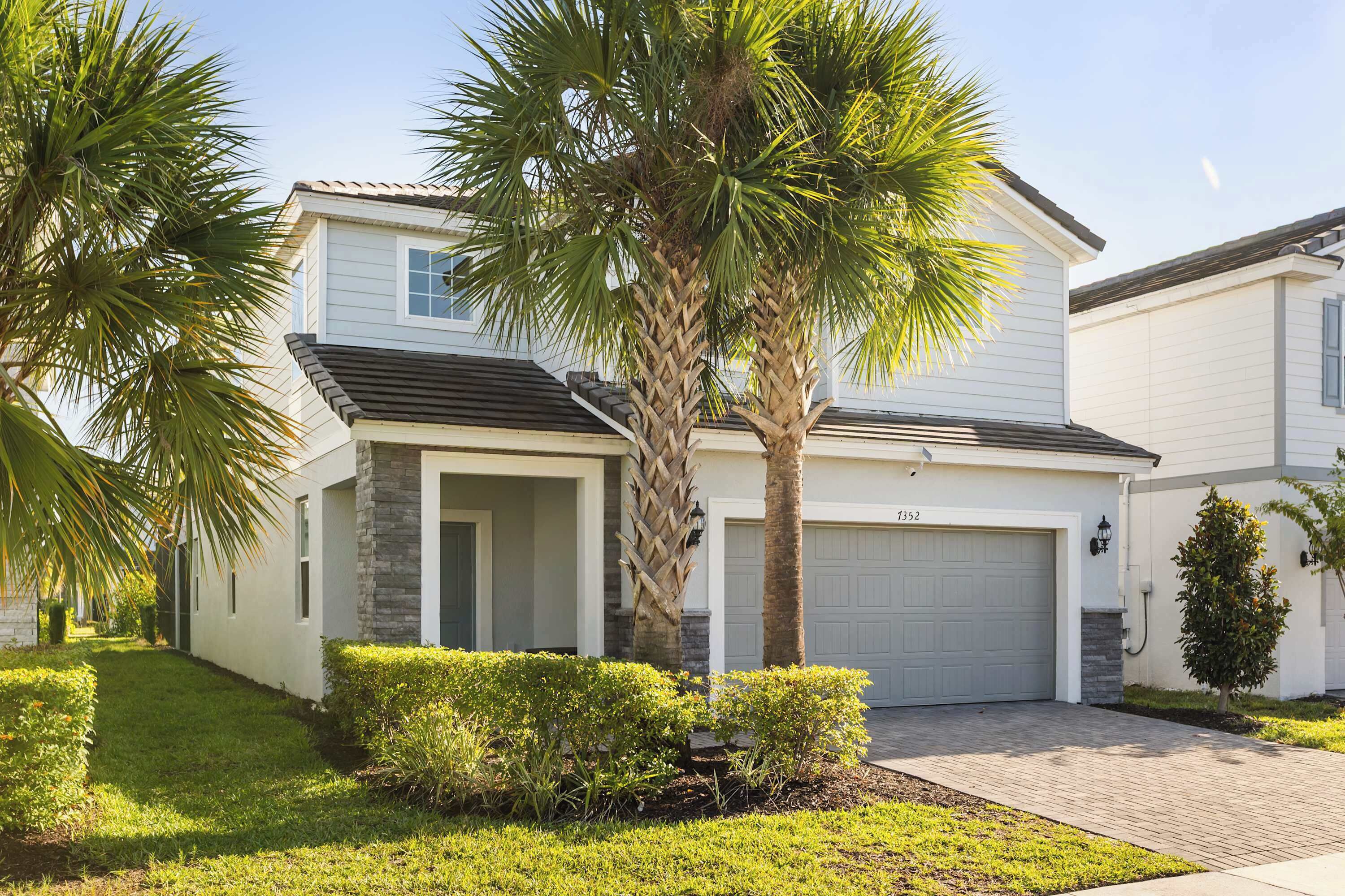 A two-story house with a garage, palm trees, and a well-maintained lawn.