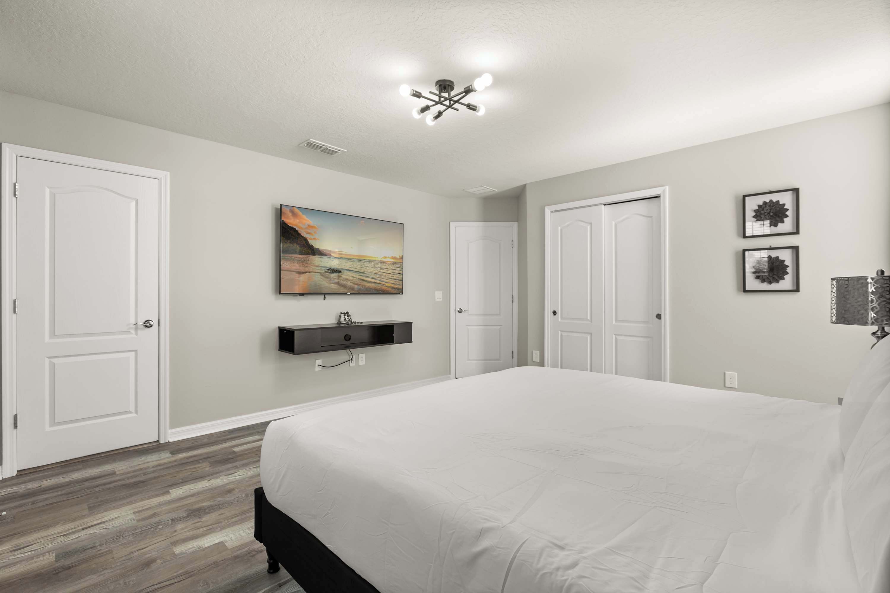 A bedroom with a large bed, white walls, a ceiling light fixture, and a painting on the wall.