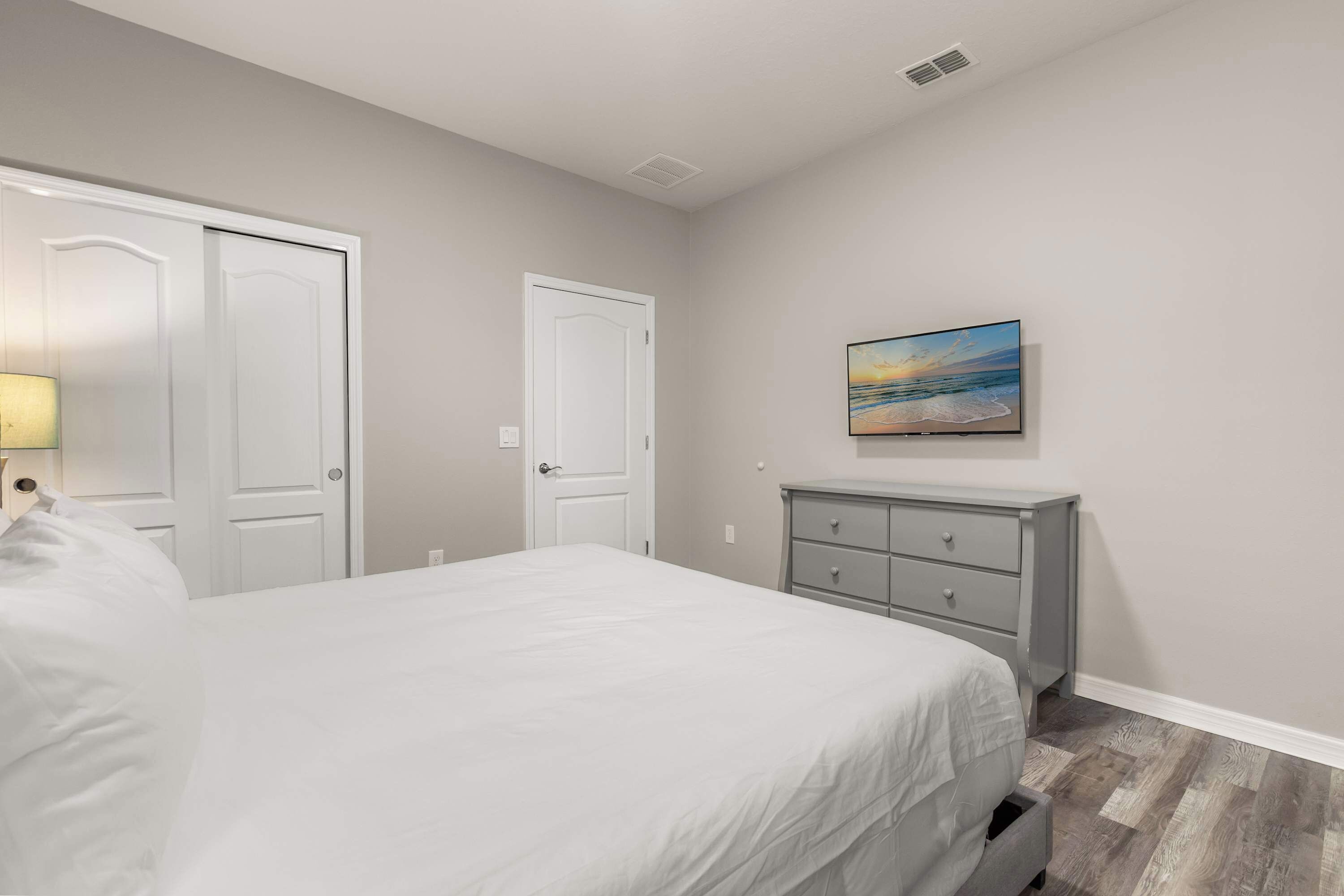 A bedroom with a bed, two doors, a dresser, and a painting on the wall.