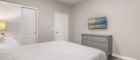 A bedroom with a bed, two doors, a dresser, and a painting on the wall.