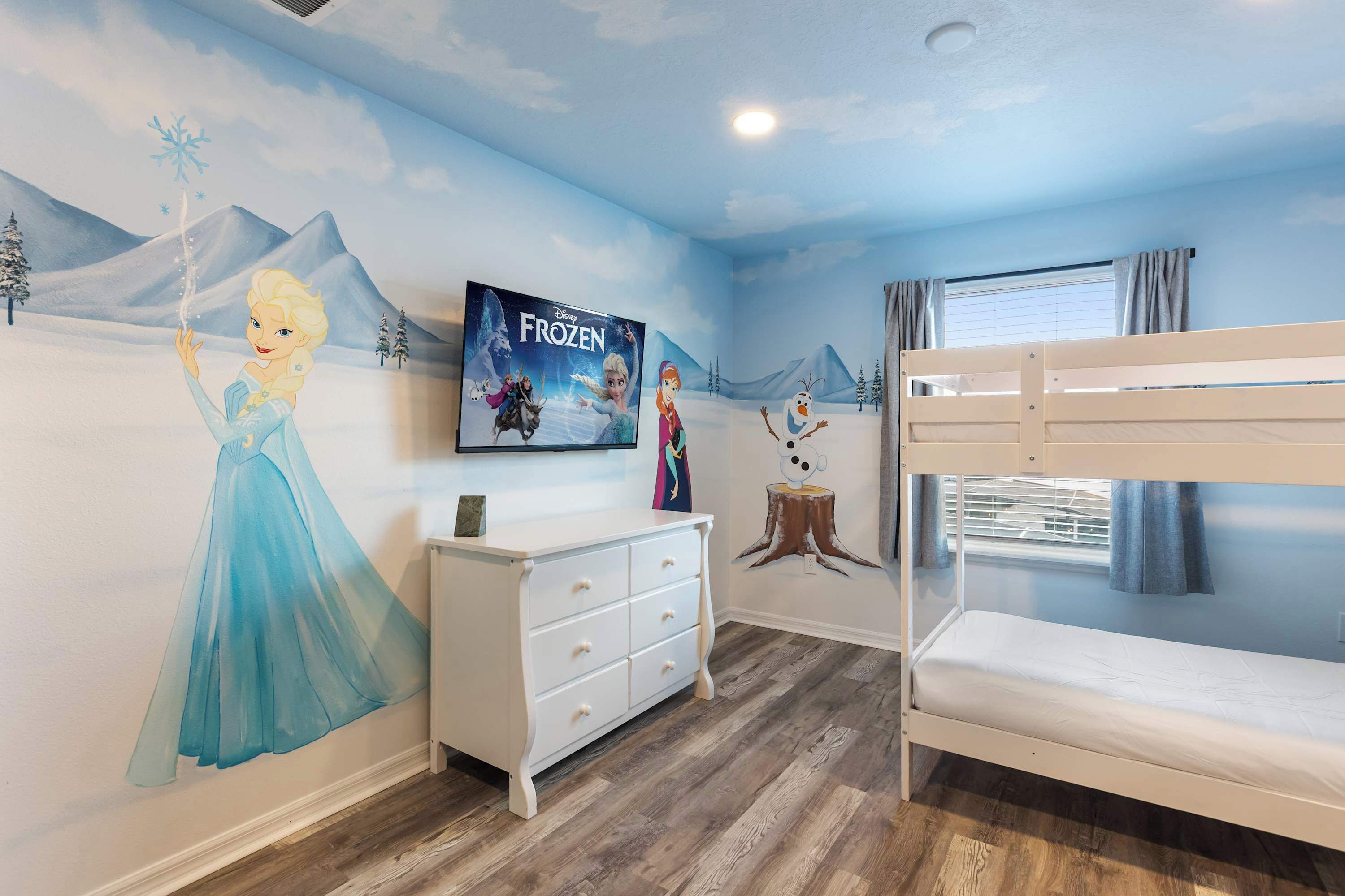 A child's bedroom with a mural of Frozen characters, a bunk bed, a dresser, and a window with curtains.
