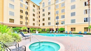 A hotel courtyard with a swimming pool, lounge chairs, and a covered seating area. - Inviting 1 Bedroom Apartment w Pool Near Disney (Orlando)
