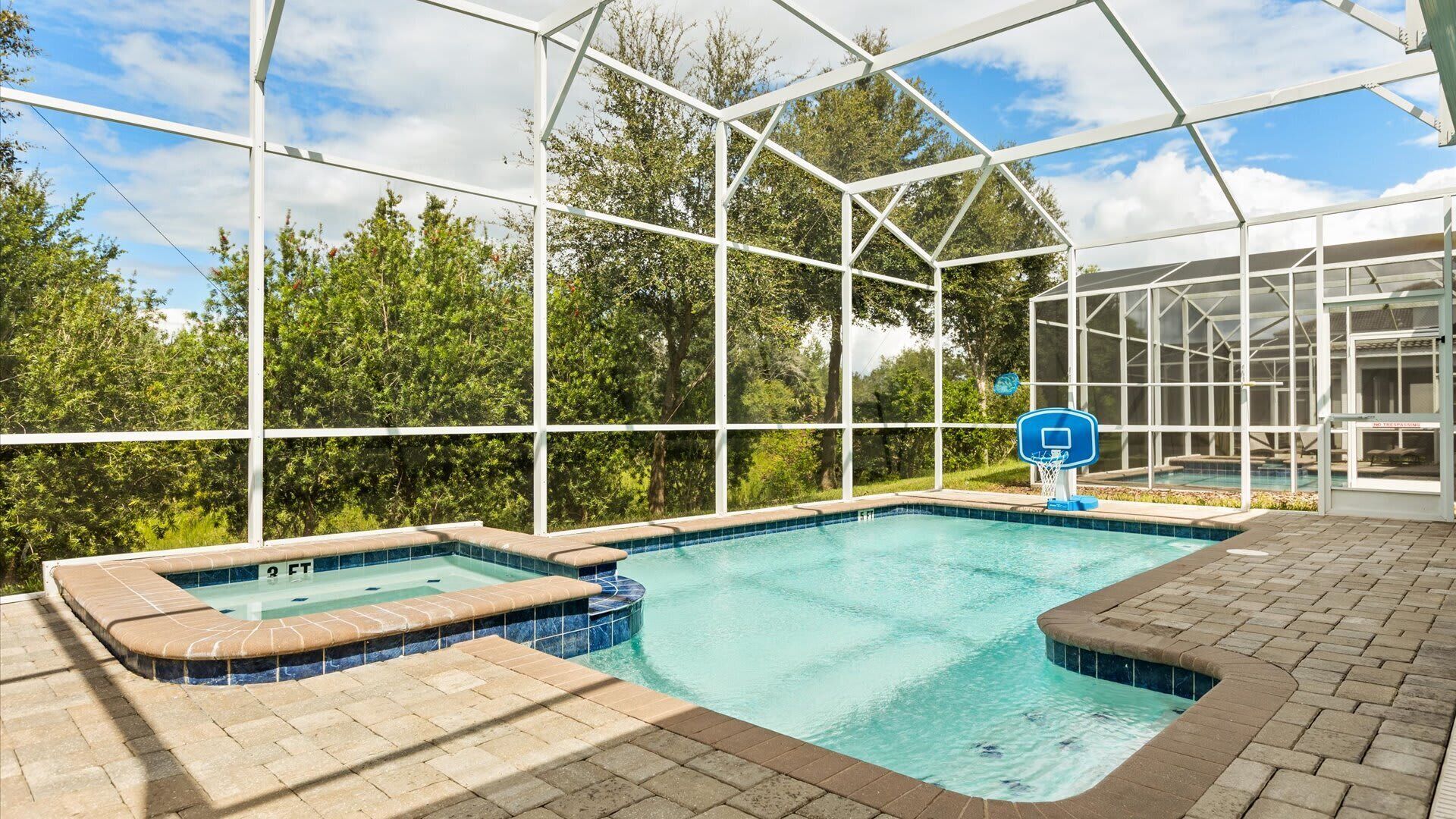 An indoor swimming pool with a hot tub, surrounded by a glass enclosure, and a basketball hoop.