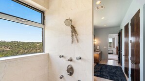 A modern bathroom with a shower, a view of the outdoors, and a dark rug on the floor. - Luxury 7BR Hill Country Gem With Barndominium (Dripping Springs)