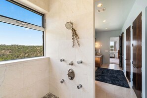 A bathroom with a shower, a window, and a view of greenery. - Luxury 7BR Hill Country Gem With Barndominium (Dripping Springs)