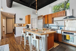 A modern kitchen with a central island, stainless steel appliances, wooden cabinets, and a large window. - Luxury 7BR Hill Country Gem With Barndominium (Dripping Springs)