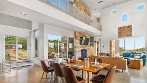 A spacious, modern interior with a large dining table, comfortable seating, and a stone fireplace. - Luxury 7BR Hill Country Gem With Barndominium (Dripping Springs)