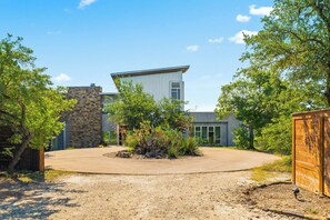 A modern building with a stone facade, a flat roof, and a paved driveway. - Luxury 7BR Hill Country Gem With Barndominium (Dripping Springs)