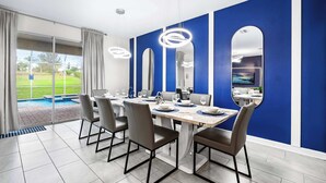 A dining area with a pool view, modern furniture, and blue accent walls. - Upstay Villa Sleeps 26 - Theater, Arcade, Pool (Davenport)