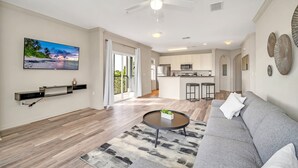 A modern living room with a grey sofa, a round coffee table, and a flat-screen TV mounted on the wall. - Condo w Pool, Games Room - Pet Friendly (Winter Garden)