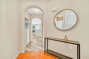 A hallway with a round mirror, a console table, and a tiled floor. - Condo w Pool, Games Room - Pet Friendly (Winter Garden)