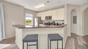 A modern kitchen with a central island, bar stools, and built-in appliances. - Condo w Pool, Games Room - Pet Friendly (Winter Garden)