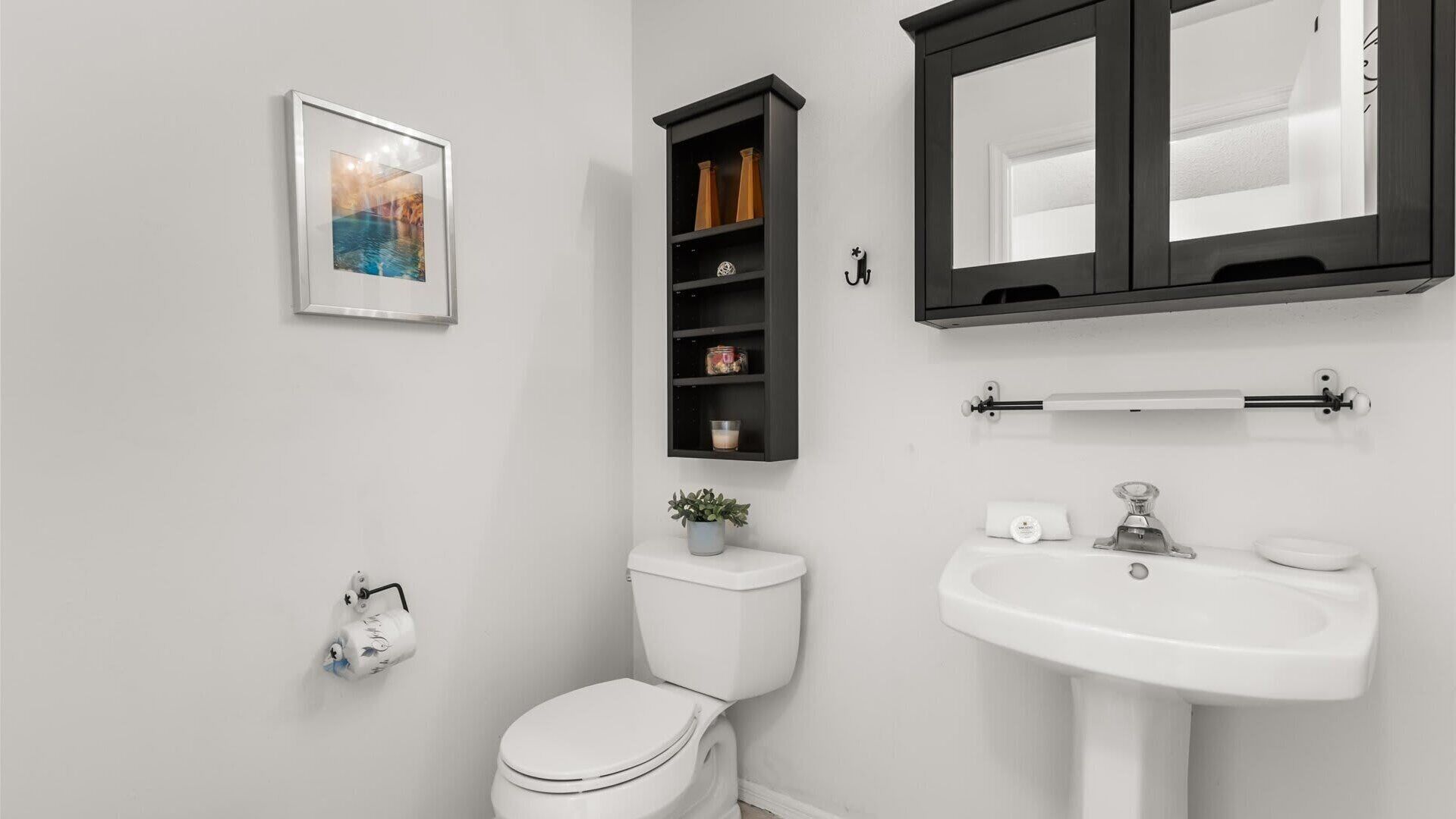 Un baño moderno con inodoro, lavamanos y un estante con artículos de aseo.