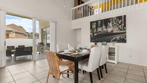 A dining area with a black table, white chairs, and a wicker chair. There is a painting on the wall and a white cabinet. - Upstay: Bright Family-friendly Retreat With Patio (Kissimmee)