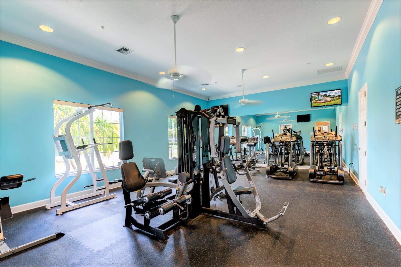 A gym with various exercise equipment, large windows, and a ceiling fan.