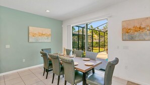 A dining area with a table set for six, six chairs, and two paintings on the walls. - Resort Home w Bbq, Pool, Games- Near Disney! (Kissimmee)