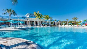 A large outdoor swimming pool with lounge chairs and umbrellas, surrounded by palm trees and modern buildings. - Upstay: Modern Windsor Resort Home Near Disney (Davenport)