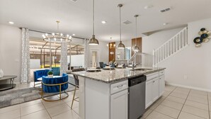 A modern kitchen with a central island, stainless steel appliances, pendant lighting, and a staircase leading to an upper level. - Upstay: Modern Windsor Resort Home Near Disney (Davenport)