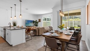 A modern kitchen with a central island, dining area with a wooden table and chairs, and a cozy seating area with a sofa and chairs. - Upstay: Luxury 4BR Family Home w Poolnear Disney (Davenport)