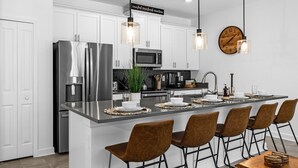A modern kitchen with white cabinets, stainless steel appliances, a central island with bar stools, pendant lighting, and a clock on the wall. - Upstay: Luxury 4BR Family Home w Poolnear Disney (Davenport)