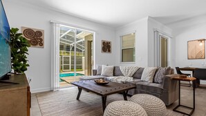 A modern living room with a sofa, coffee table, ottomans, and a TV on a wooden cabinet. - Upstay: Luxury 4BR Family Home w Poolnear Disney (Davenport)