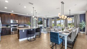 Una cocina moderna con armarios oscuros, una isla central y un comedor con una mesa larga y sillas.