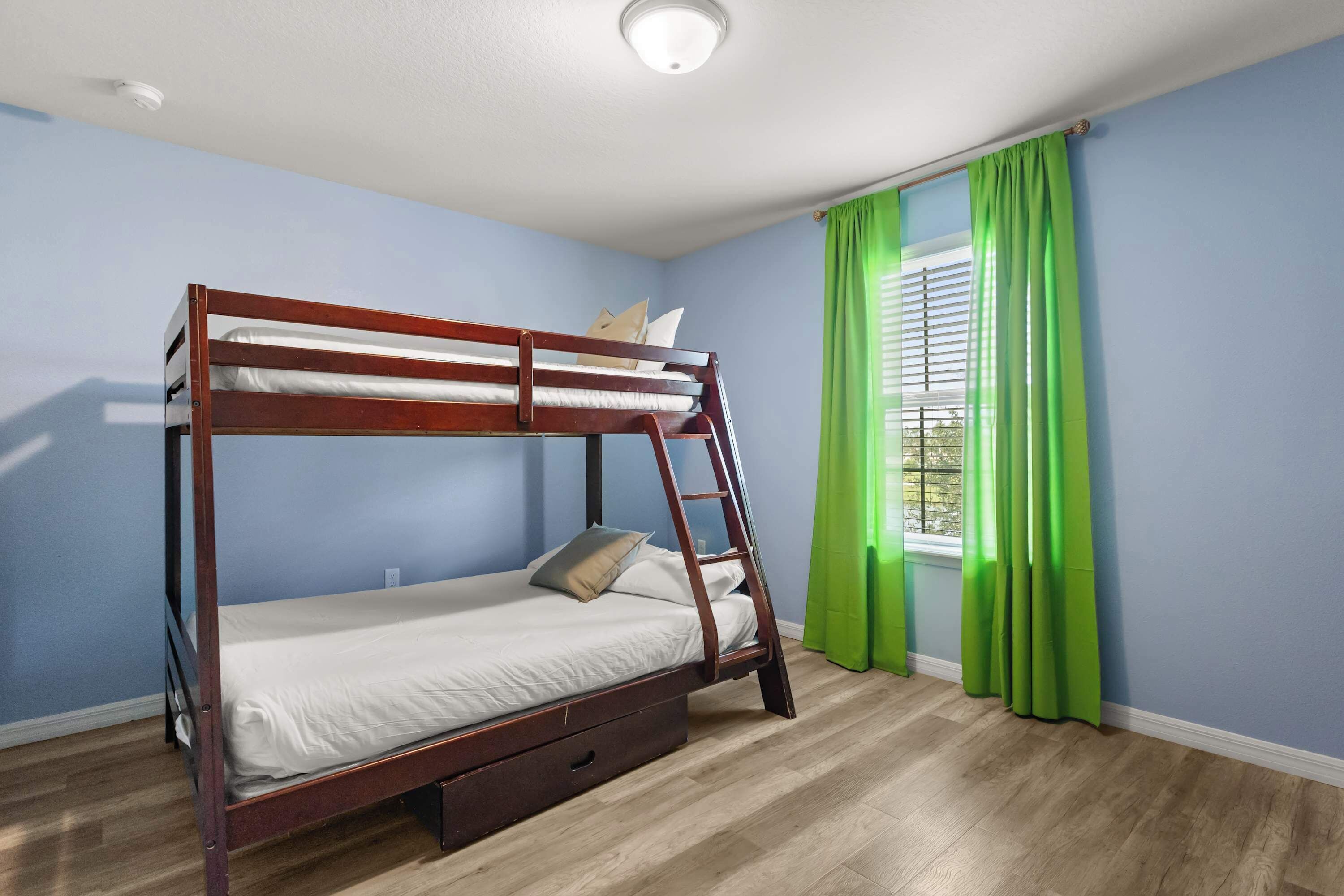 Une chambre avec un lit superposé, une échelle, une fenêtre avec des rideaux verts et un interrupteur sur le mur.