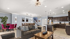 A modern living room with a sofa, coffee table, and dining area. There is a staircase leading to an upper level. - Upstay Family Retreat w Pool, Theater & Games Room (Kissimmee)