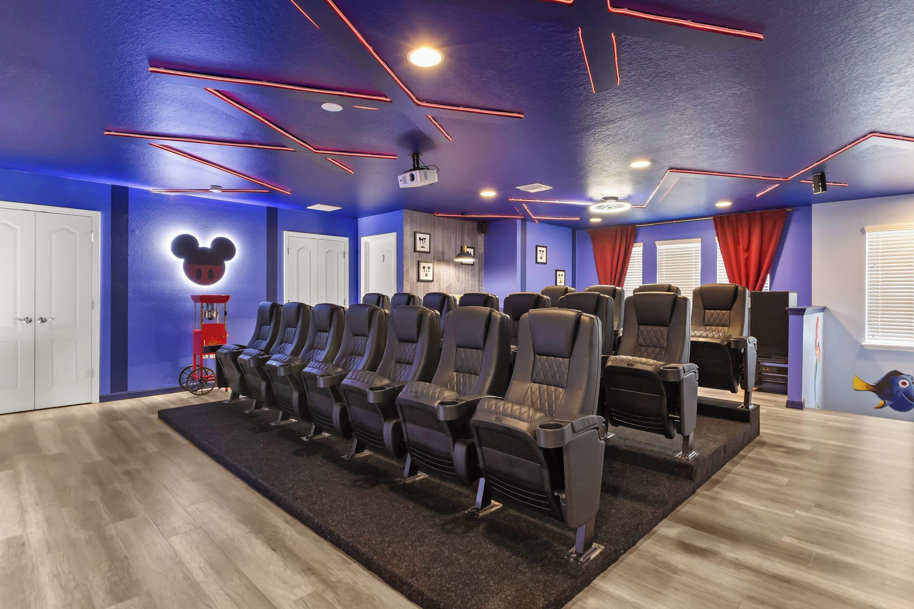 Ein Heimkino mit einer Reihe schwarzer Ledersessel, einem roten Vorhang und einem beleuchteten Mickey-Mouse-Schild an der Wand.