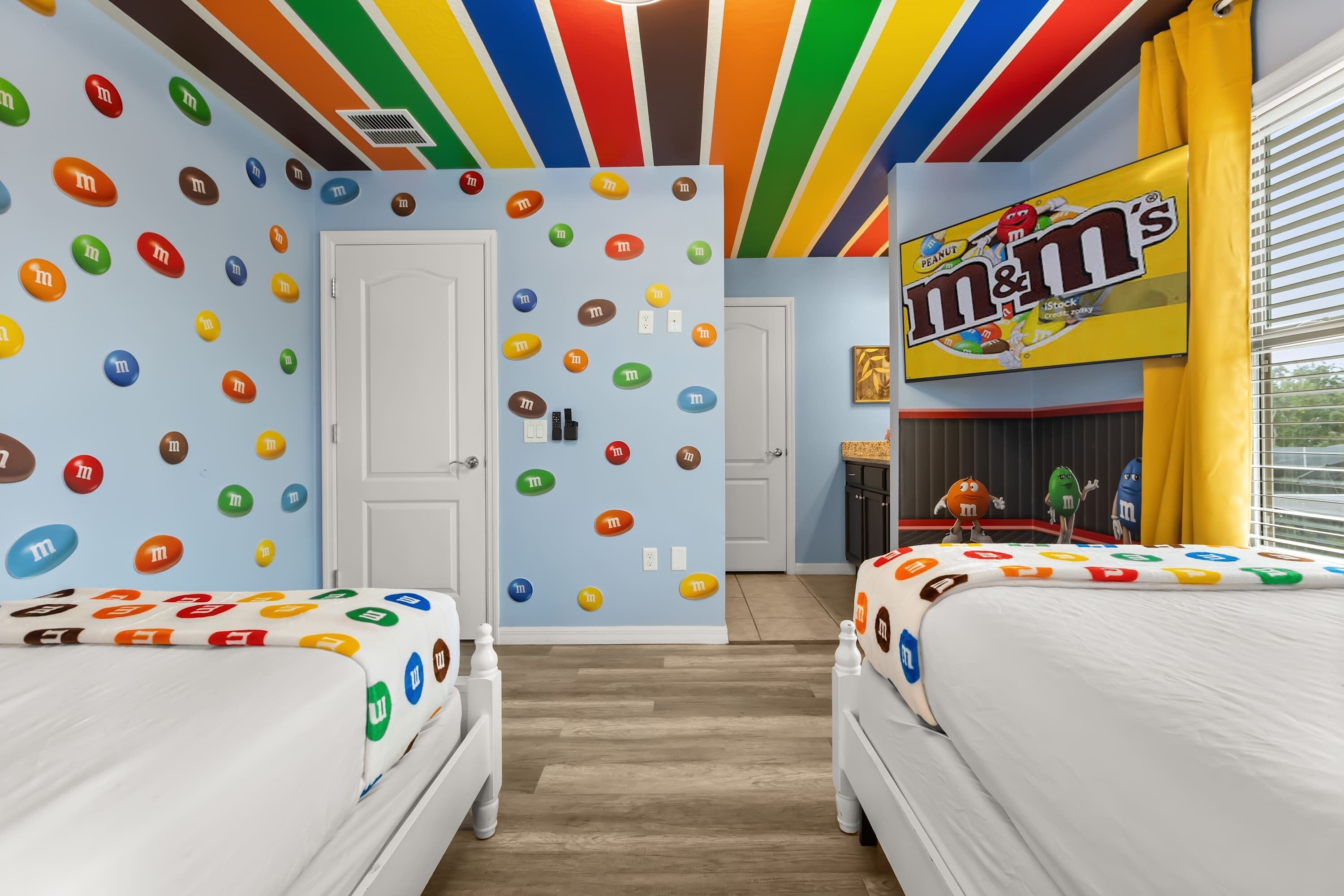 A room with two beds, a wall decorated with candy icons, and a large M&M's sign.
