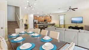 A dining area with a table set for six, a kitchen in the background, a ceiling fan, and a TV mounted on the wall. - Upstay: Family Home w Pool & Cinemachampionsgate (Davenport)