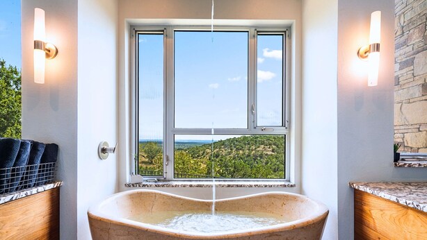 A freestanding bathtub with a view of a landscape through a window. - Luxury Hilltop Villa With Hot Tub & Scenic Views (Dripping Springs)