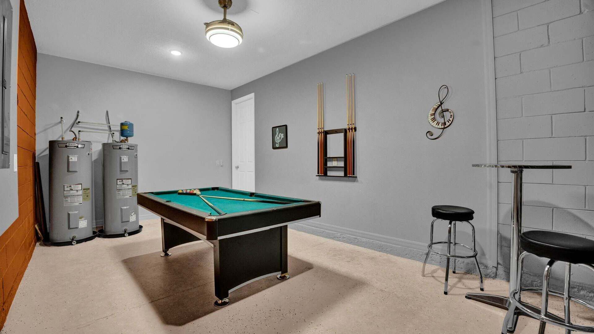 A pool table in a room with a grey brick wall, two heaters, a mirror, and a treble clef decoration.