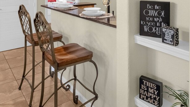Una cocina con barra, sillas de madera, lámparas de mimbre colgantes y estantes con objetos decorativos.