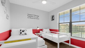 Un dormitorio con dos camas, una decoración en tonos rojo y blanco, un ventilador de techo y una ventana con persianas.