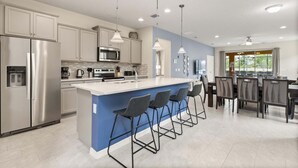 Una cocina moderna con una isla central, taburetes de bar, electrodomésticos de acero inoxidable y un comedor con vistas.
