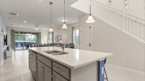Una cocina moderna con una isla grande, electrodomésticos de acero inoxidable e iluminación colgante.