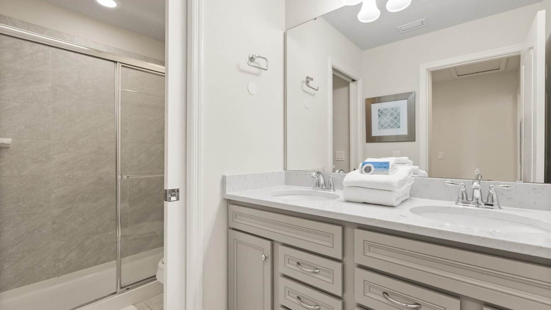 A modern bathroom with a walk-in shower, a large mirror, and a vanity with a sink and multiple drawers.