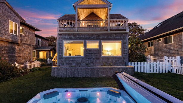 Een tweelaags huis met een balkon, een jacuzzi en een witte picket fence.