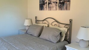 Een slaapkamer met een bed, twee nachtkastjes en drie abstracte schilderijen aan de muur.