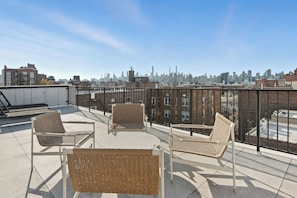 A rooftop terrace with wicker furniture and a city skyline view. - Elegant Studio Apartment in the Heart of Astoria (ASTORIA)