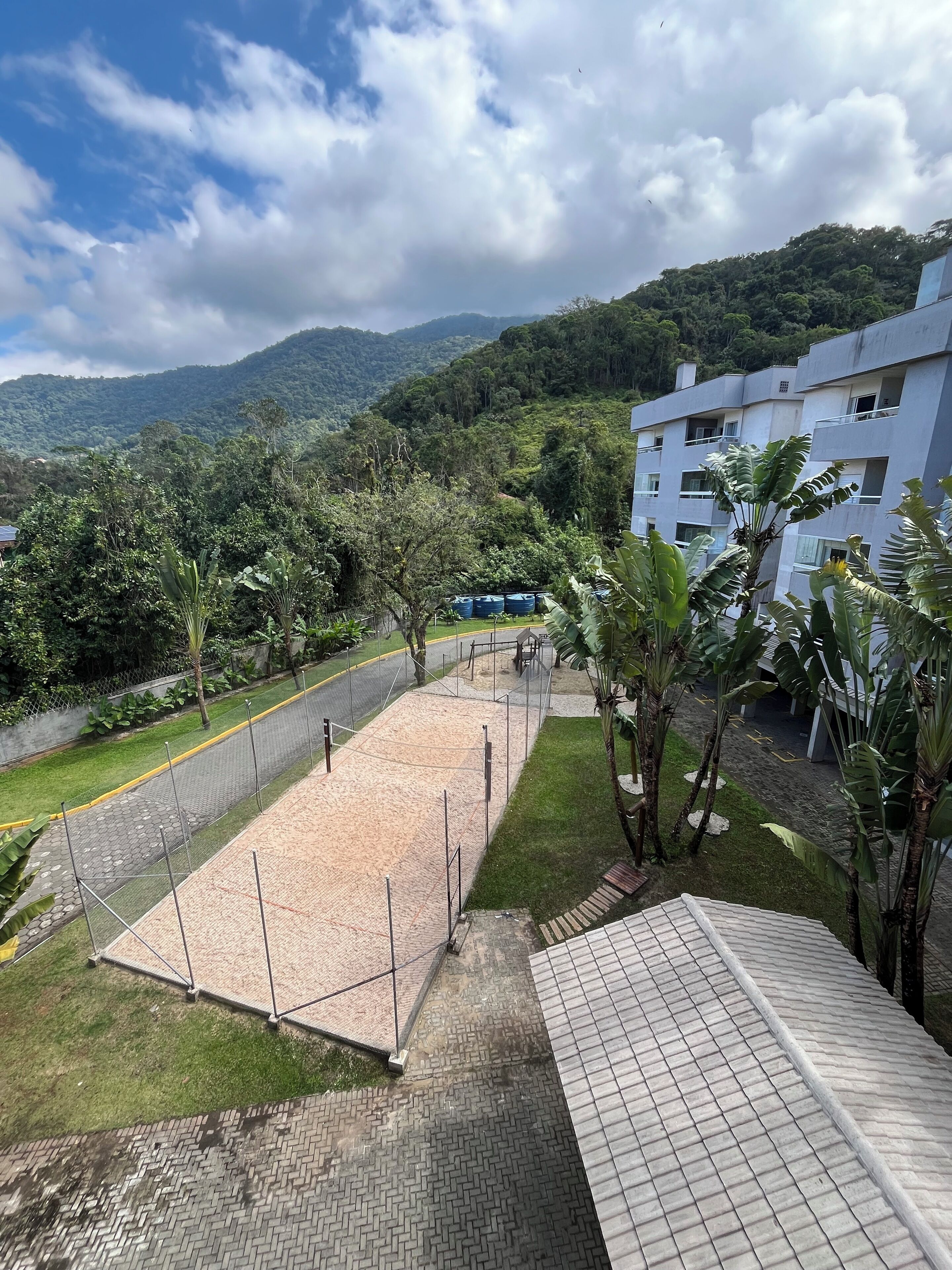 Une cour avec une zone pavée, entourée de verdure et d’un bâtiment doté de nombreux balcons.