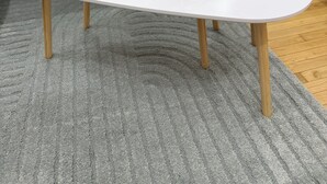 A white table with a vase of white flowers on a grey rug.