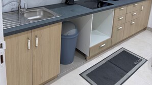 A modern kitchen with wooden cabinets, a black countertop, a sink, a trash bin, and a microwave.