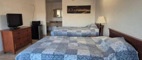 Une chambre avec deux lits, une télévision, une commode et un tableau au mur.