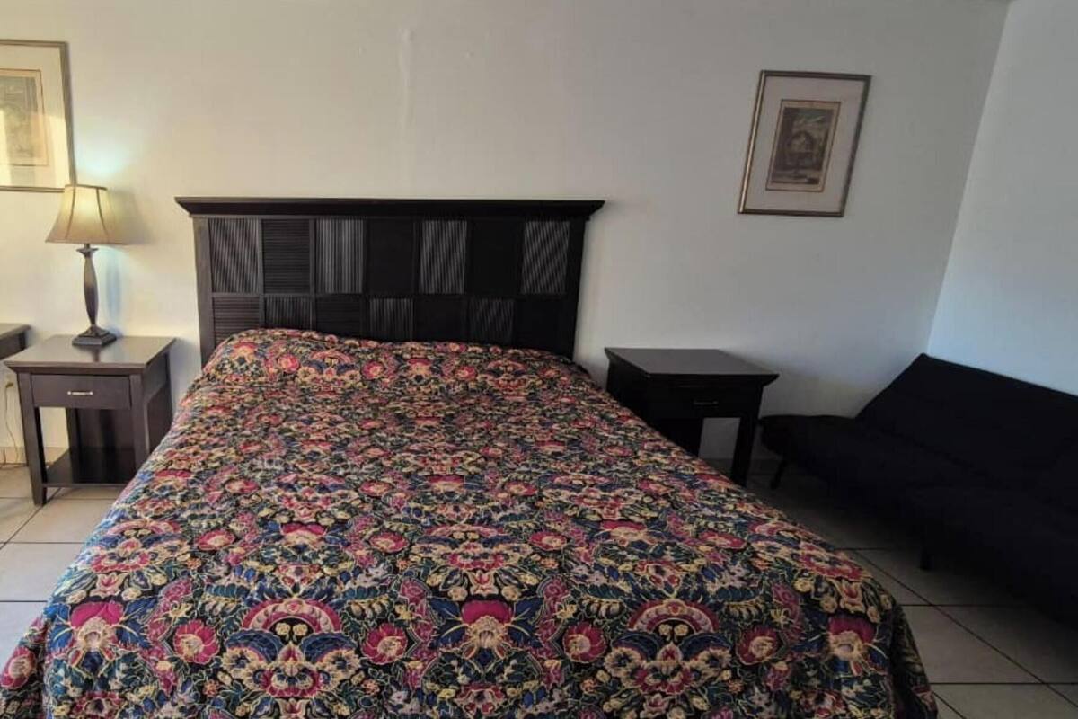 Ein Schlafzimmer mit einem großen Bett, einem Nachttisch, einer Lampe und einem gerahmten Bild an der Wand.